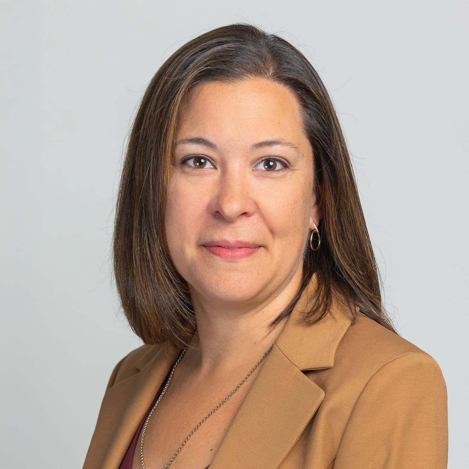 Professional headshot of a woman in a brown blazer against a light background, smiling.
