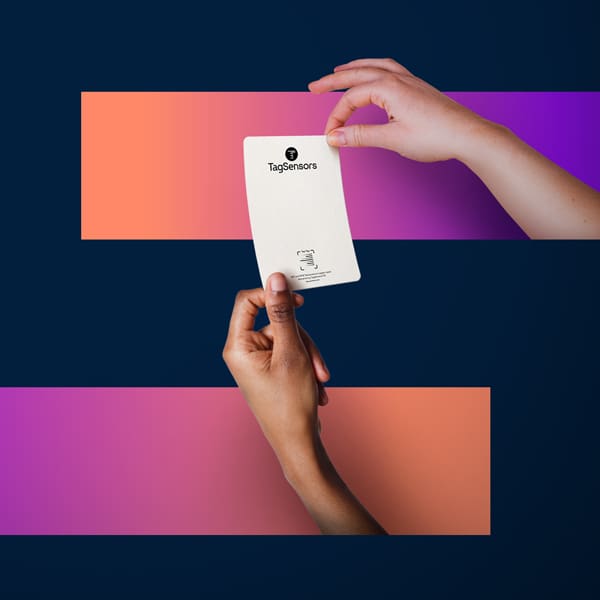 Two hands holding a white business card with "TagSensors" logo against colorful geometric background